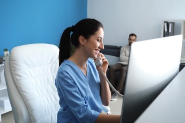 Woman in medical scrubs on phone and laptop