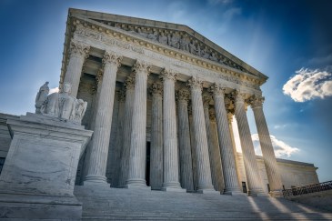 The Supreme Court building looms over the camera, the sky blue behind it.