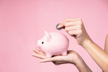 Woman pointing a coin into a piggy bank