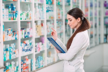 Female pharmacist with clipboard standing in front of medications