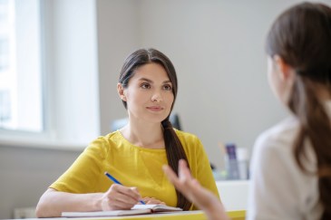 Psychologist in a yellow shirt taking notes with a patient in the foreground
