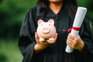 College graduate holding a diploma and a piggy bank in her hand