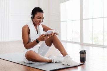 Woman wearing headphones with phone exercising on yoga mat, smiling