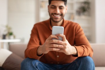Man holding his phone in front of him while sitting on a couch.