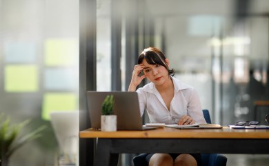 Woman sitting at desk with head on hand, looking concerned