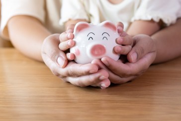 Parent and child with hands together around a piggybank