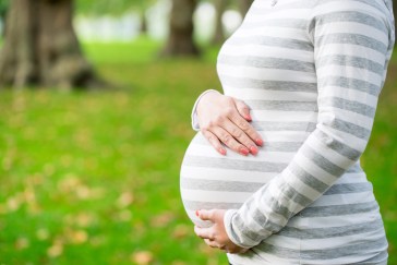 Pregnant woman standing outside holding belly
