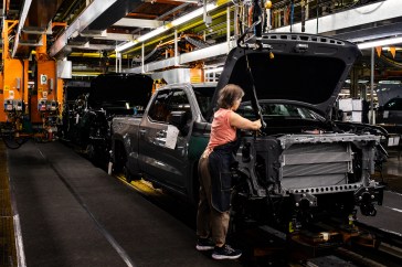 A woman is working on the construction of a large black truck in a factory; She is focused on the trunk.