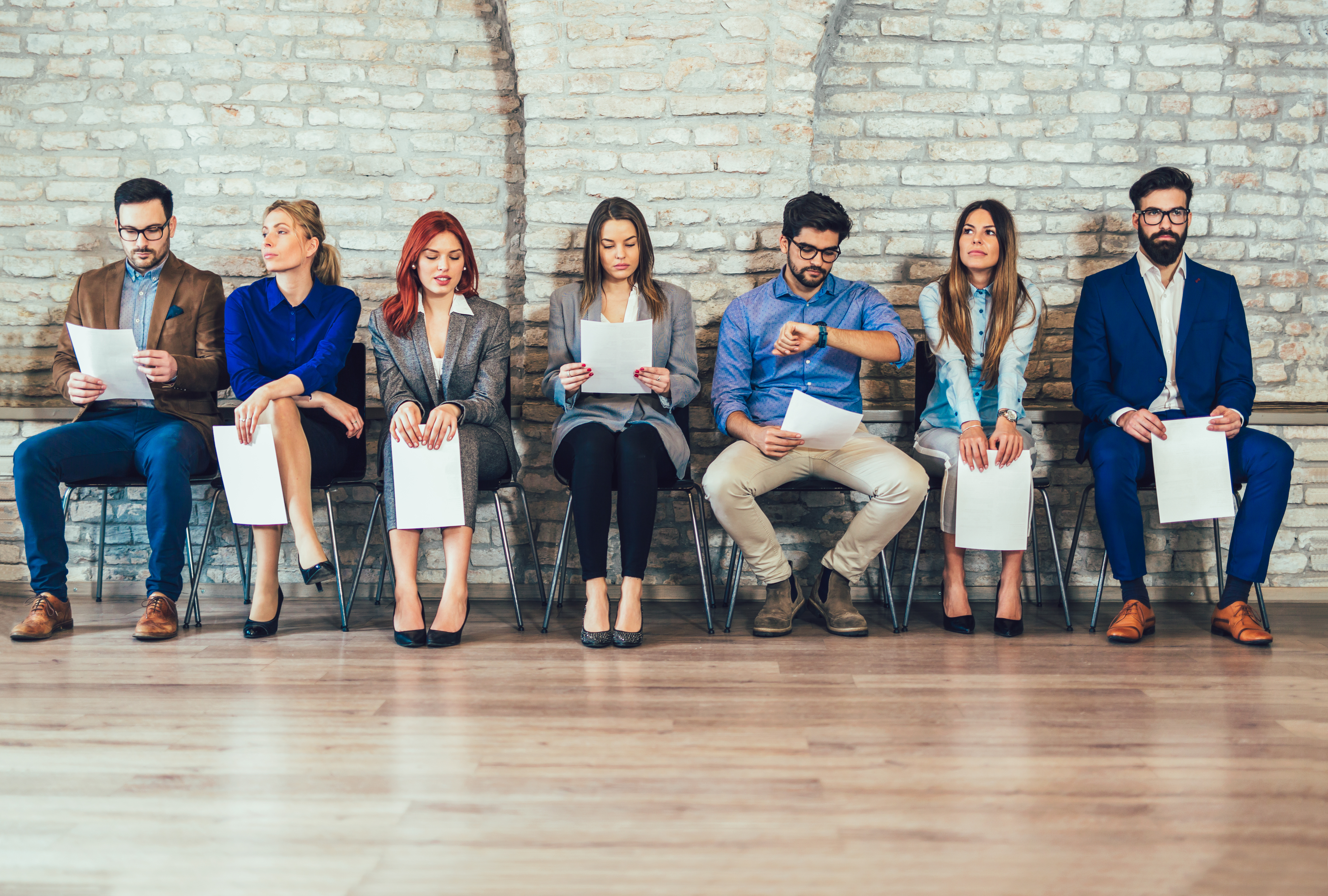 Job candidates sitting waiting for interview with resumes