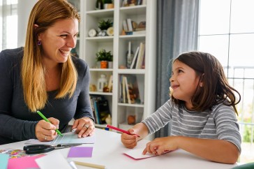 Mother and daughter working at table together writing on paper and smiling