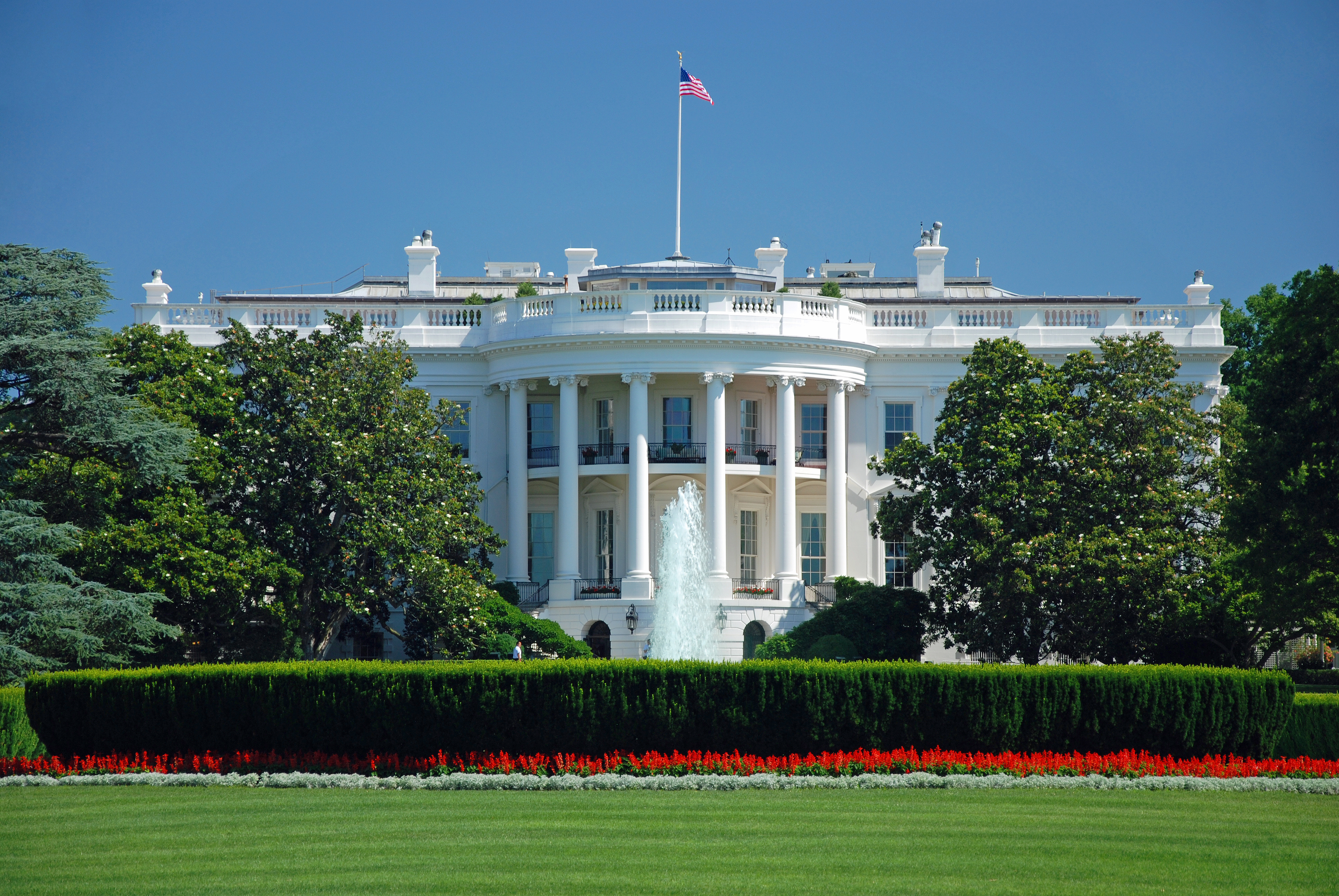 The White House, colonial mansion bordered by green trees and a manicured lawn.