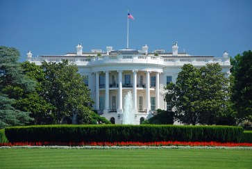 The White House, colonial mansion bordered by green trees and a manicured lawn.