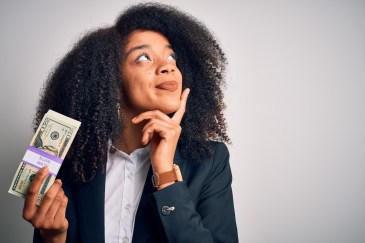 Woman holding stack of money, one hand on chin, thinking