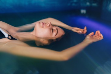 A woman in a back and white swimsuit is floating in water glowing with blue light.