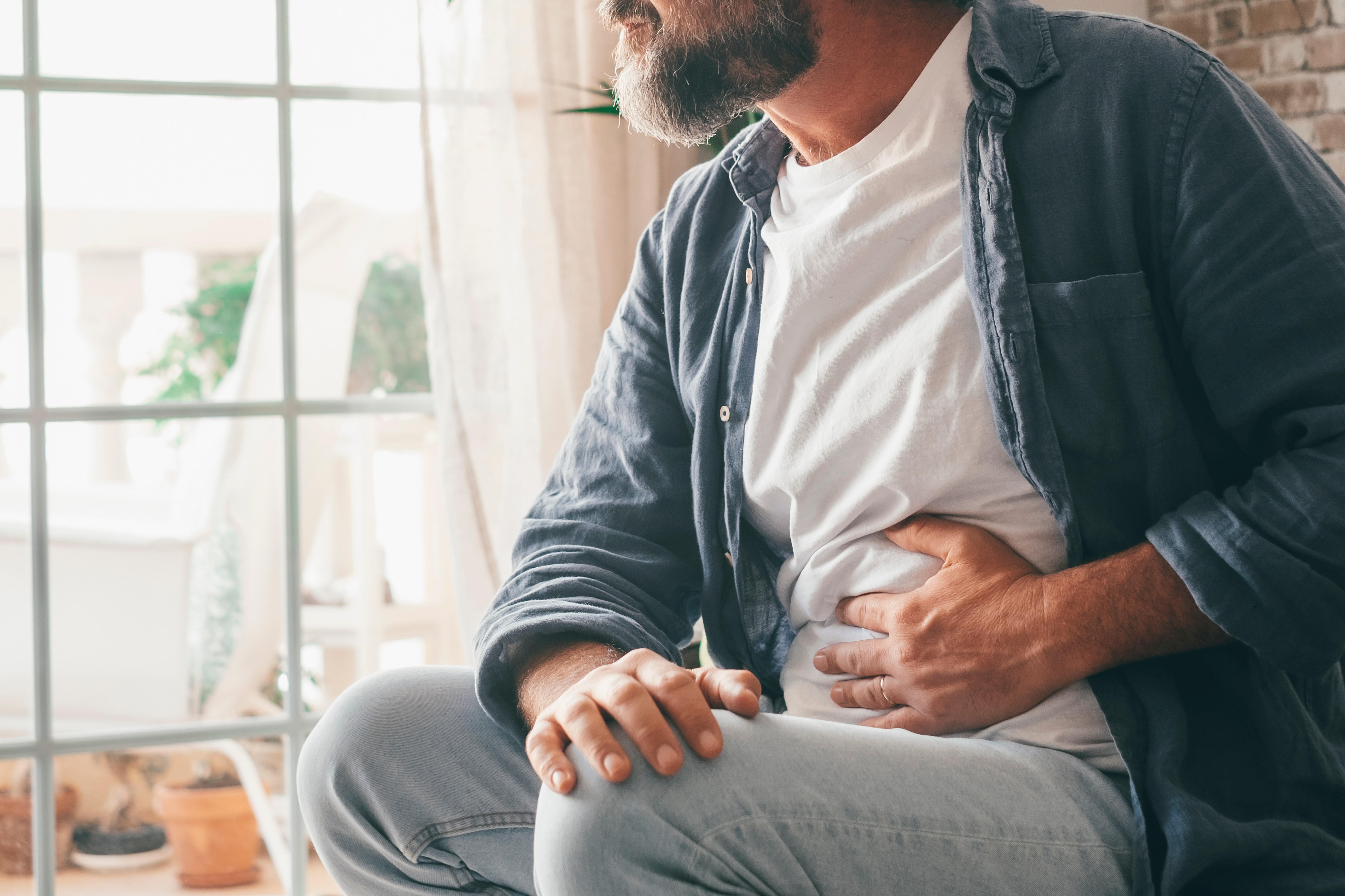 Man sitting next to window holding stomach