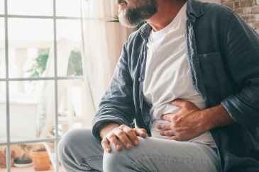 Man sitting next to window holding stomach