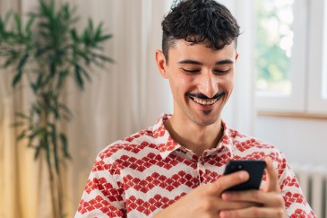 Young man with a mustache typing on his cell phone and smiling