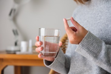 Woman's hand holding a pill and other hand holding a water cup
