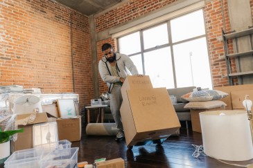 Man moving a cart with moving boxes stacked on it into an apartment