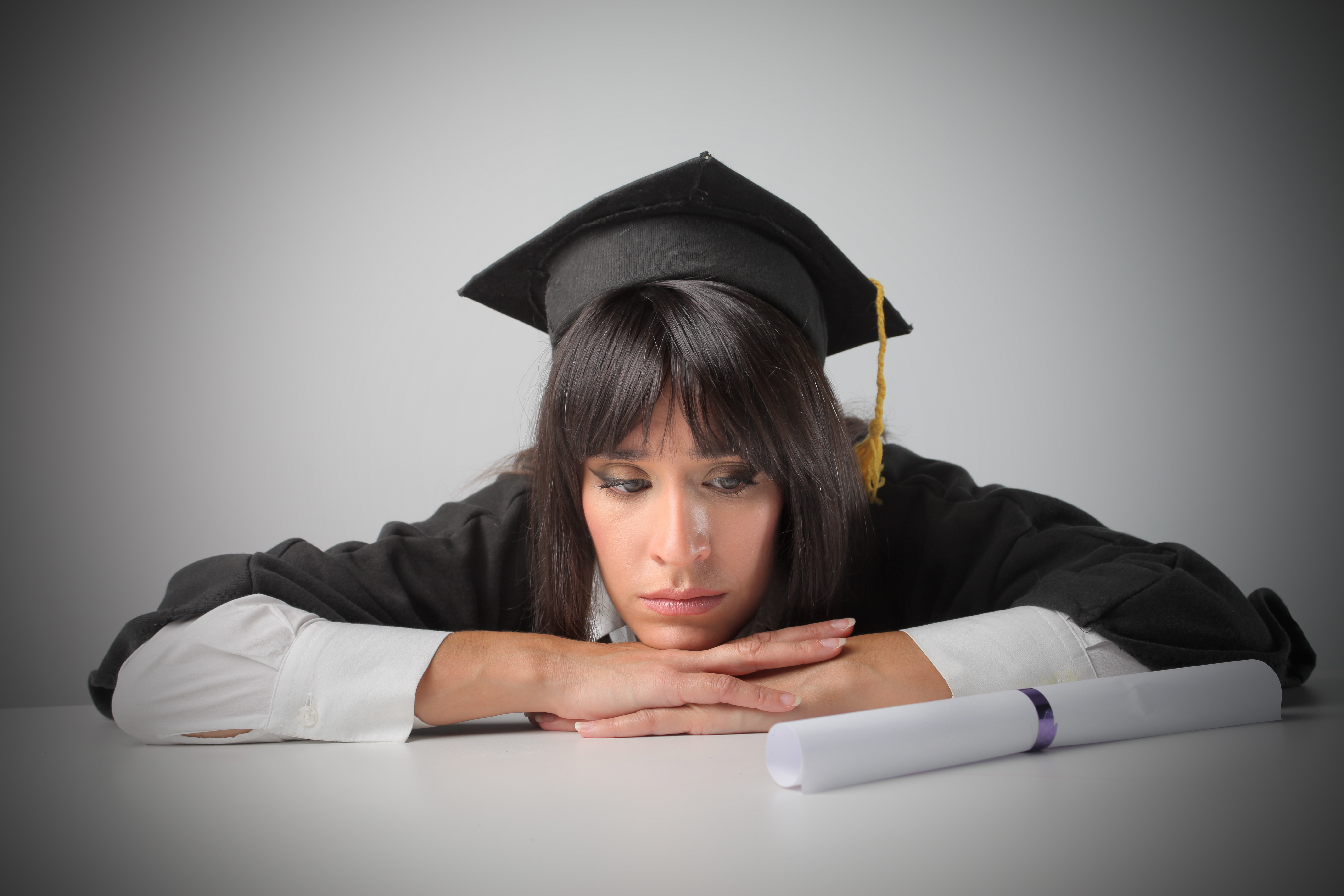 Woman college graduate looking at diploma sad
