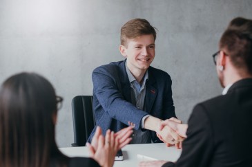 Young man shaking hands with man across table; job interview