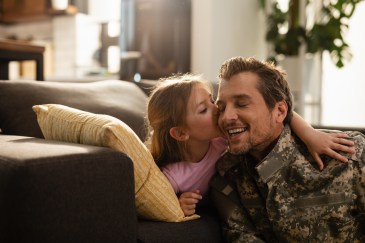 Man in fatigue uniform with daughter who is kissing his cheek