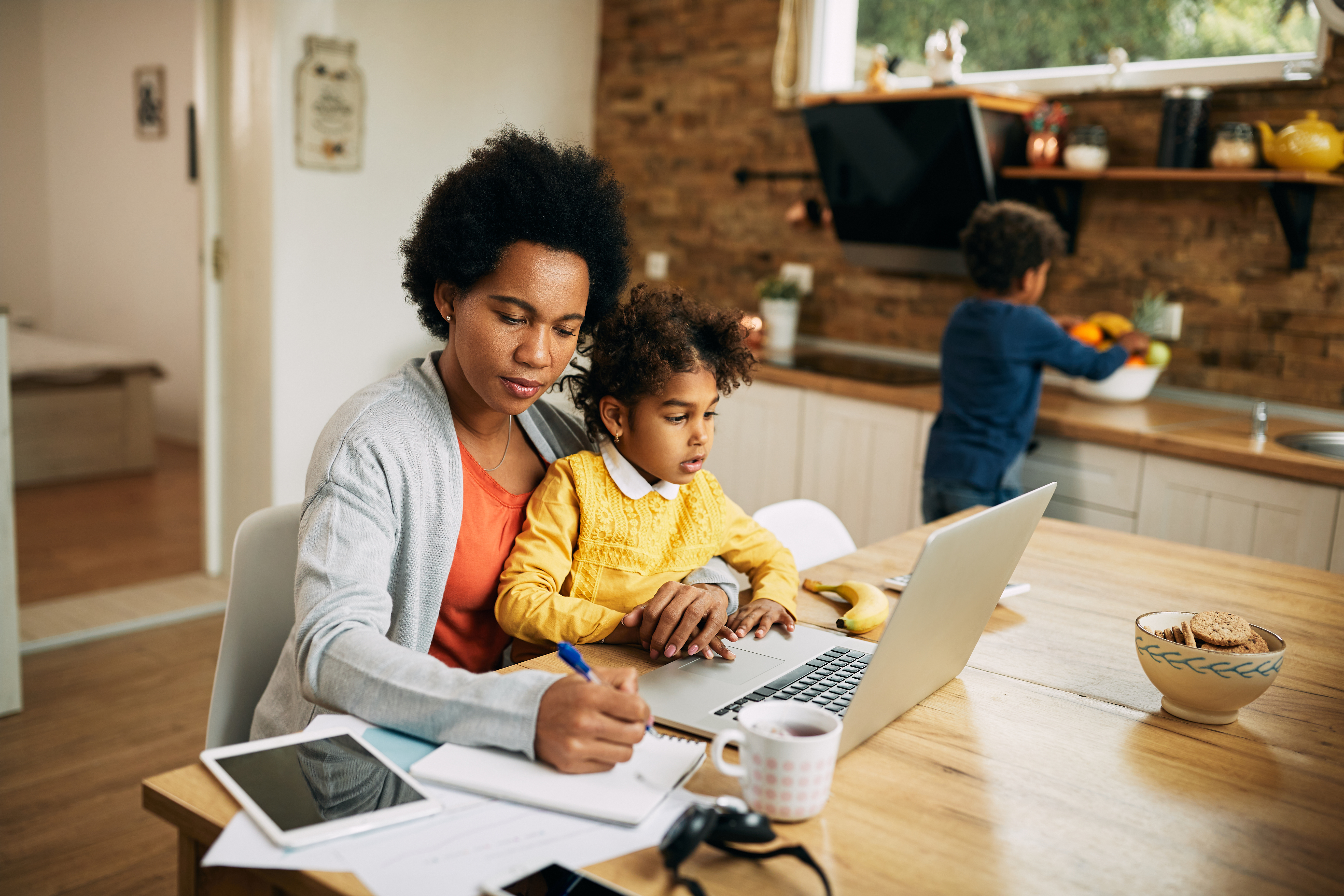 Mom holding young child in lap while working on laptop and writing