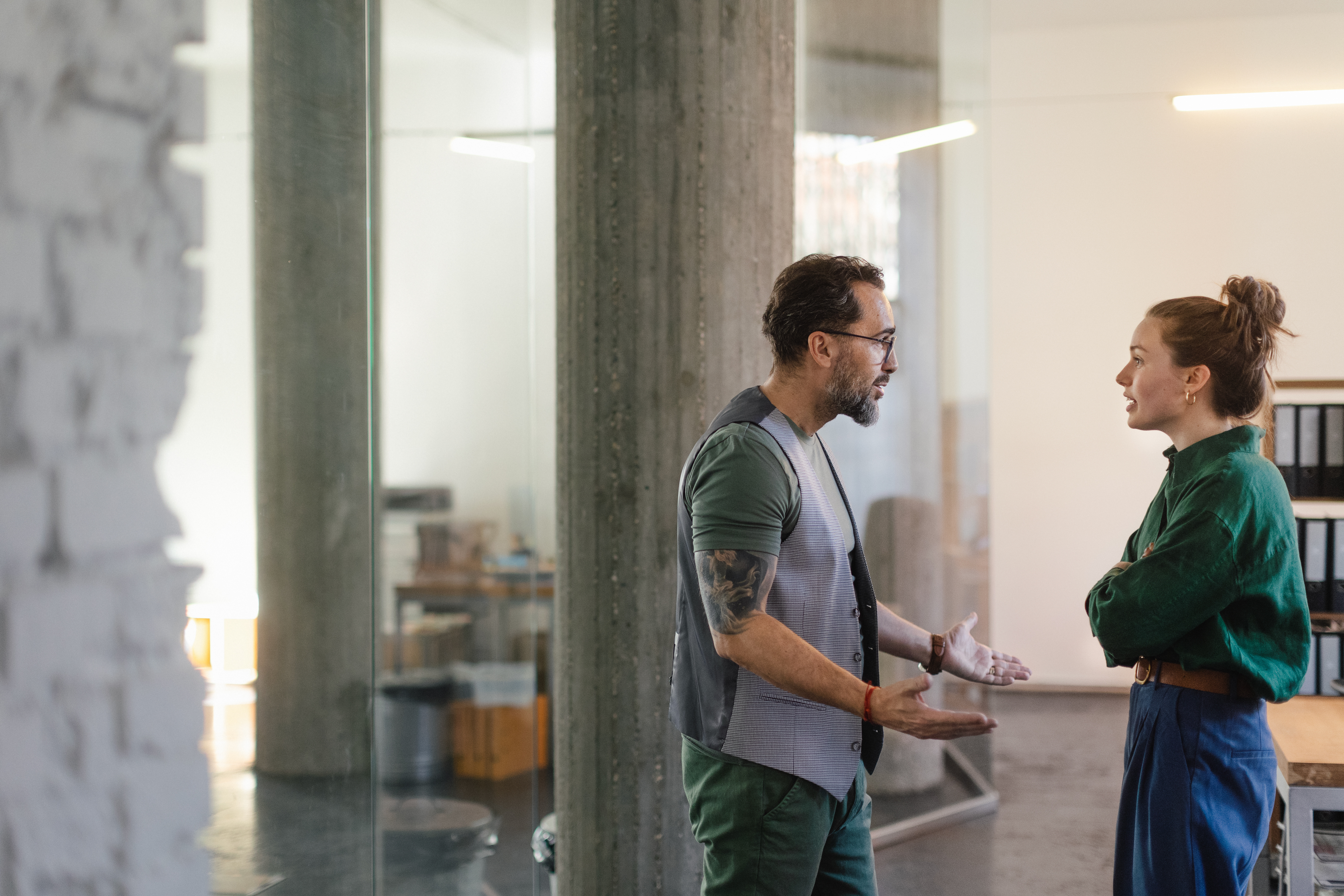 Two colleagues look like they're in mid-argument while standing near a desk in the office.