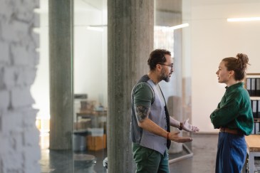 Two colleagues look like they're in mid-argument while standing near a desk in the office.