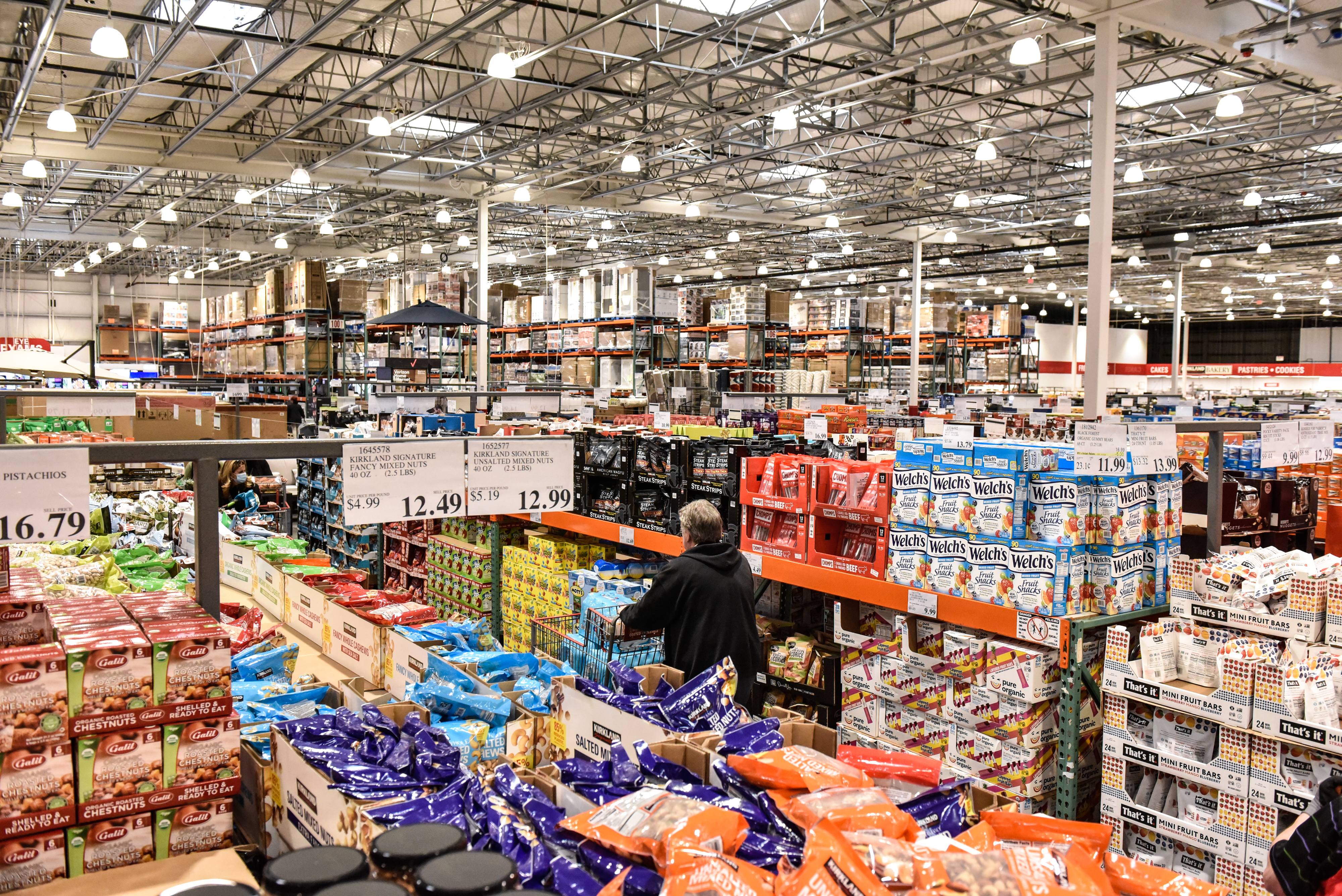 A man is pushing her cart through Costco's snack foods aisle.
