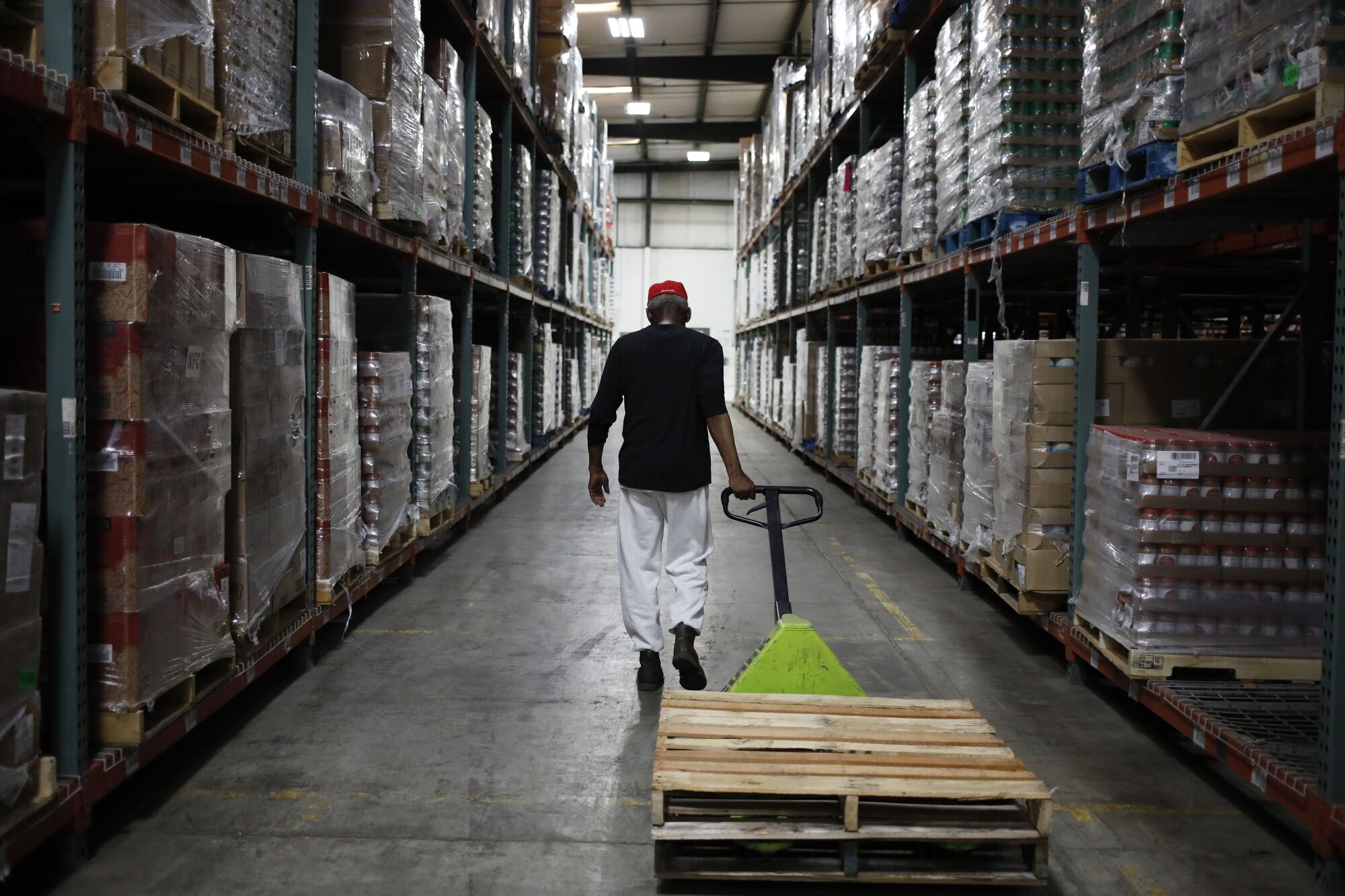 Worker in warehouse pulling pallet on wheels down aisle
