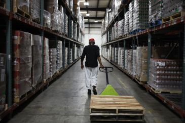 Worker in warehouse pulling pallet on wheels down aisle