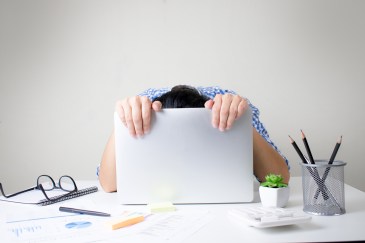 Person hanging their head behind a laptop screen