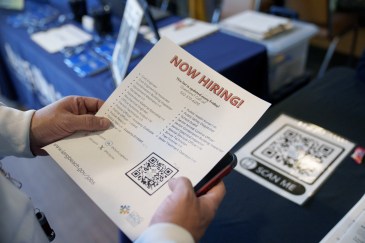 A man holding a piece of paper that says "Now Hiring."