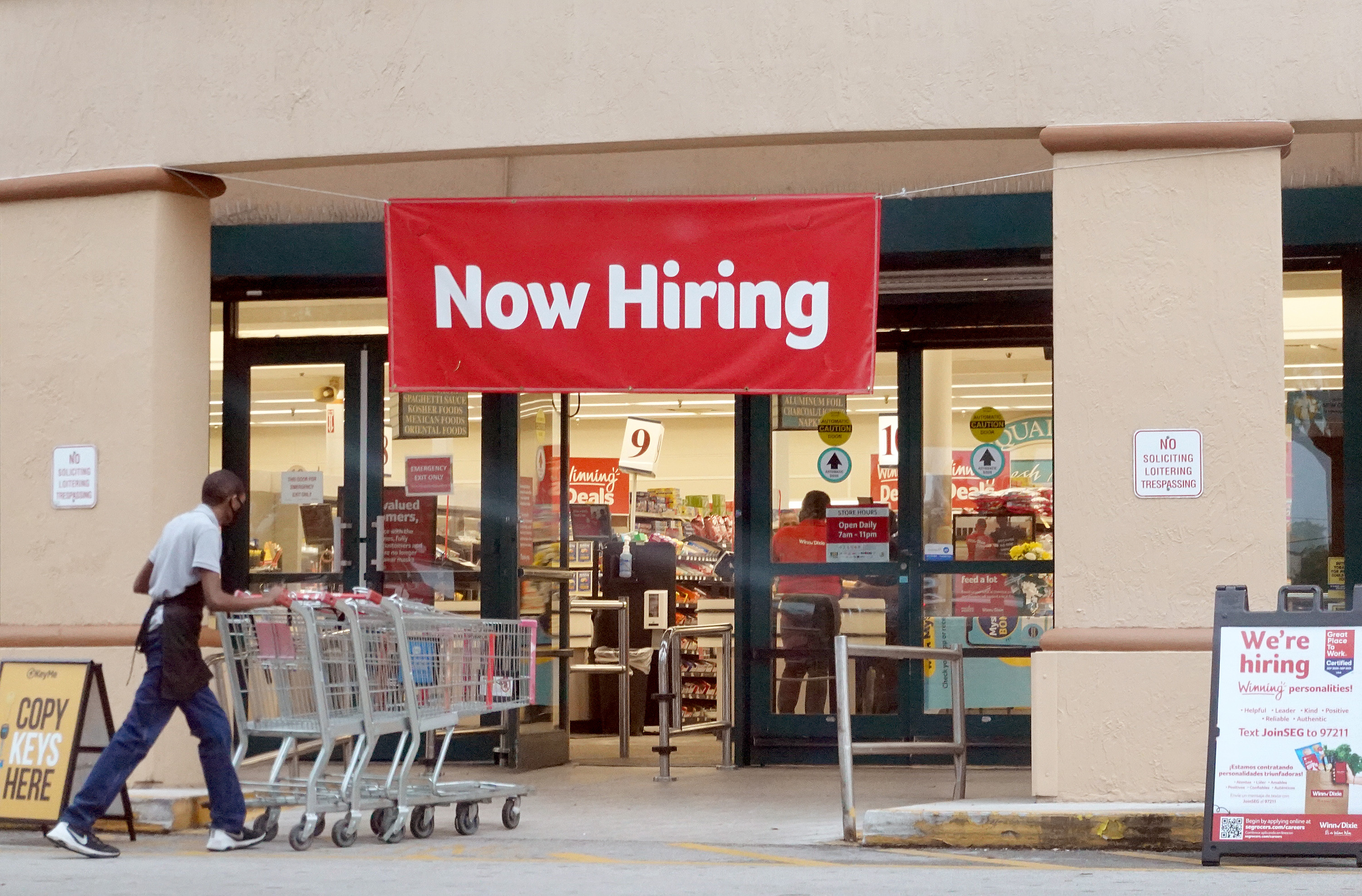 A 'Now Hiring" sign at the front of a grocery store.