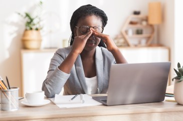 Woman sitting at desk with laptop hands on eyes stressed out tired