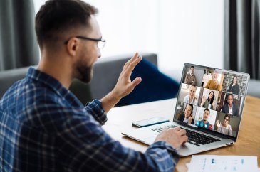 A man is on a Zoom call and waving at his laptop.