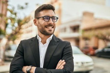 Man standing outside in business suit, wearing glasses, smiling, arms crossed