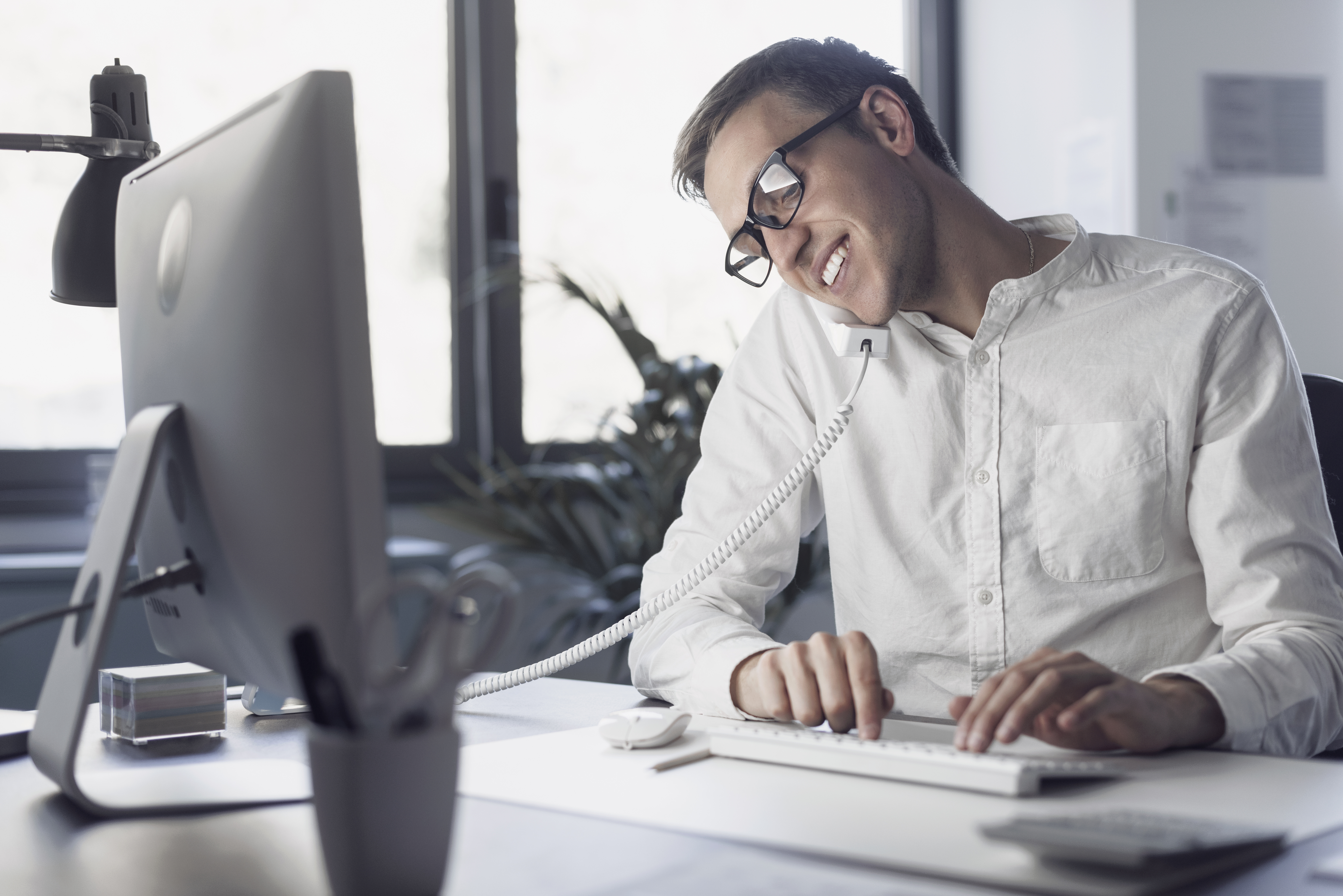 Man sitting at desk with desktop computer on phone smiling