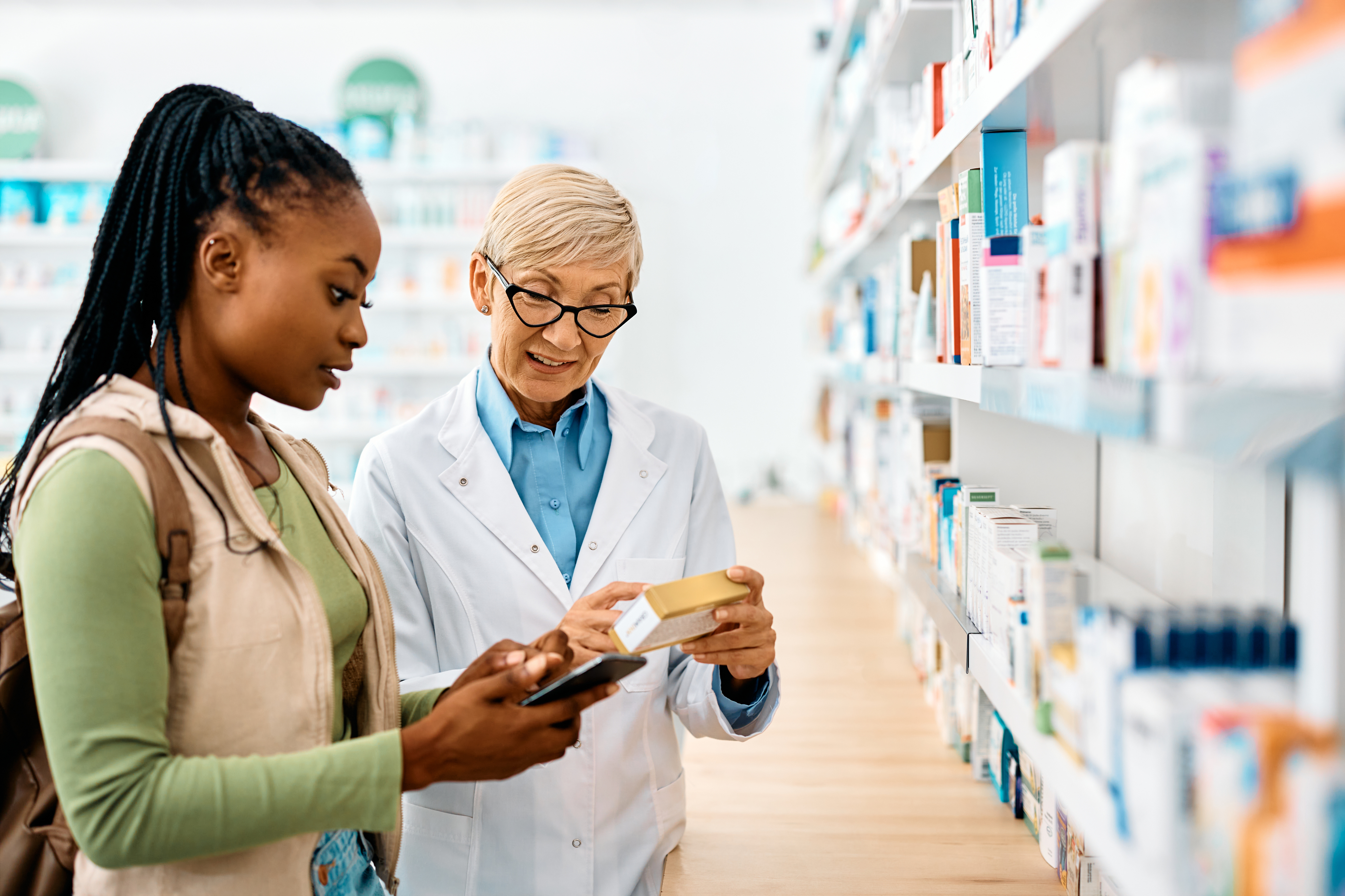 Young woman standing with older female pharmacist looking at medication