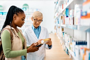 Young woman standing with older female pharmacist looking at medication