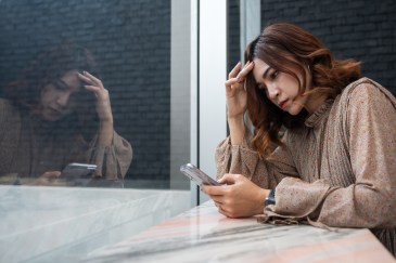 Young woman looking at phone worried hand on head