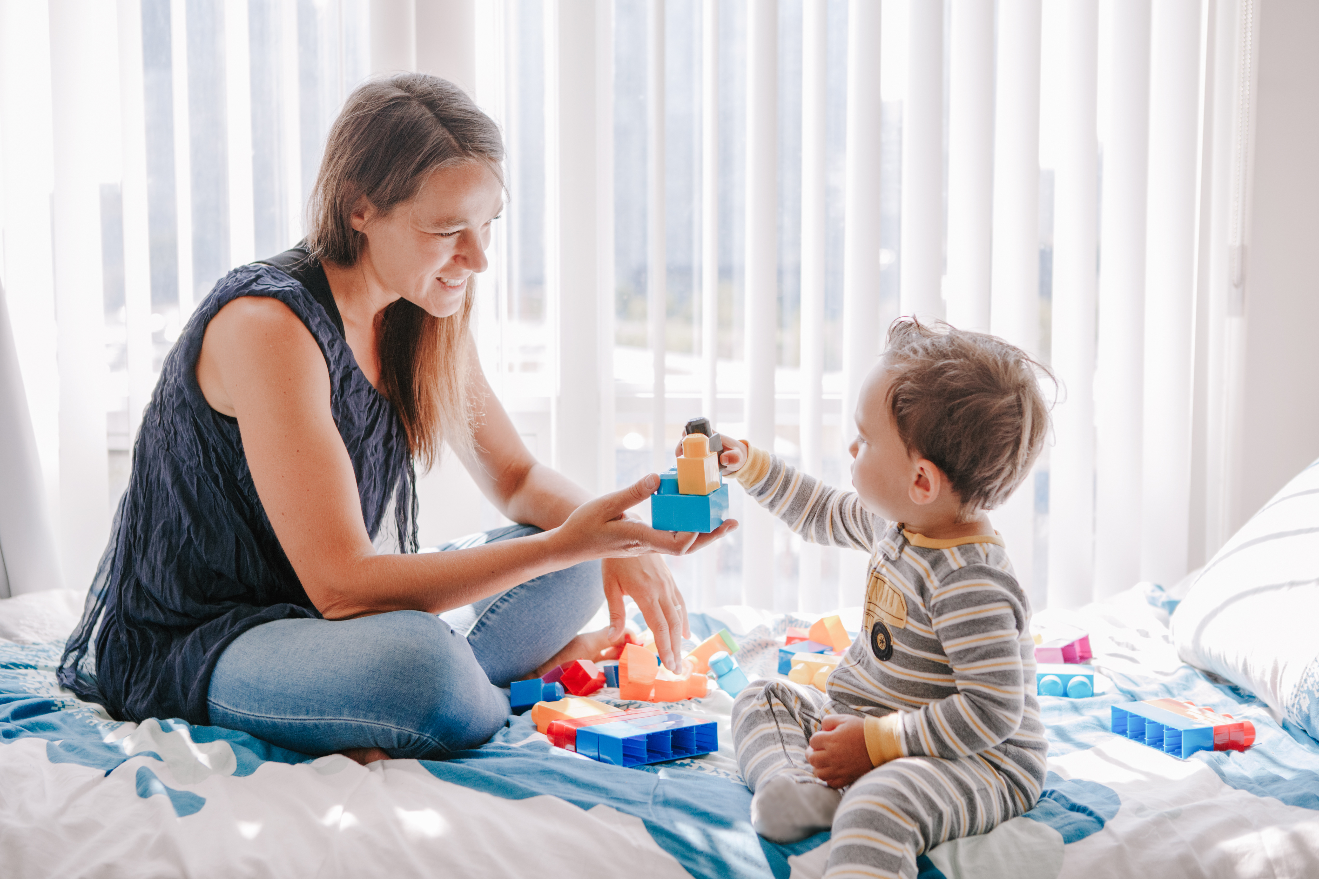 Mother playing blocks with child on bed
