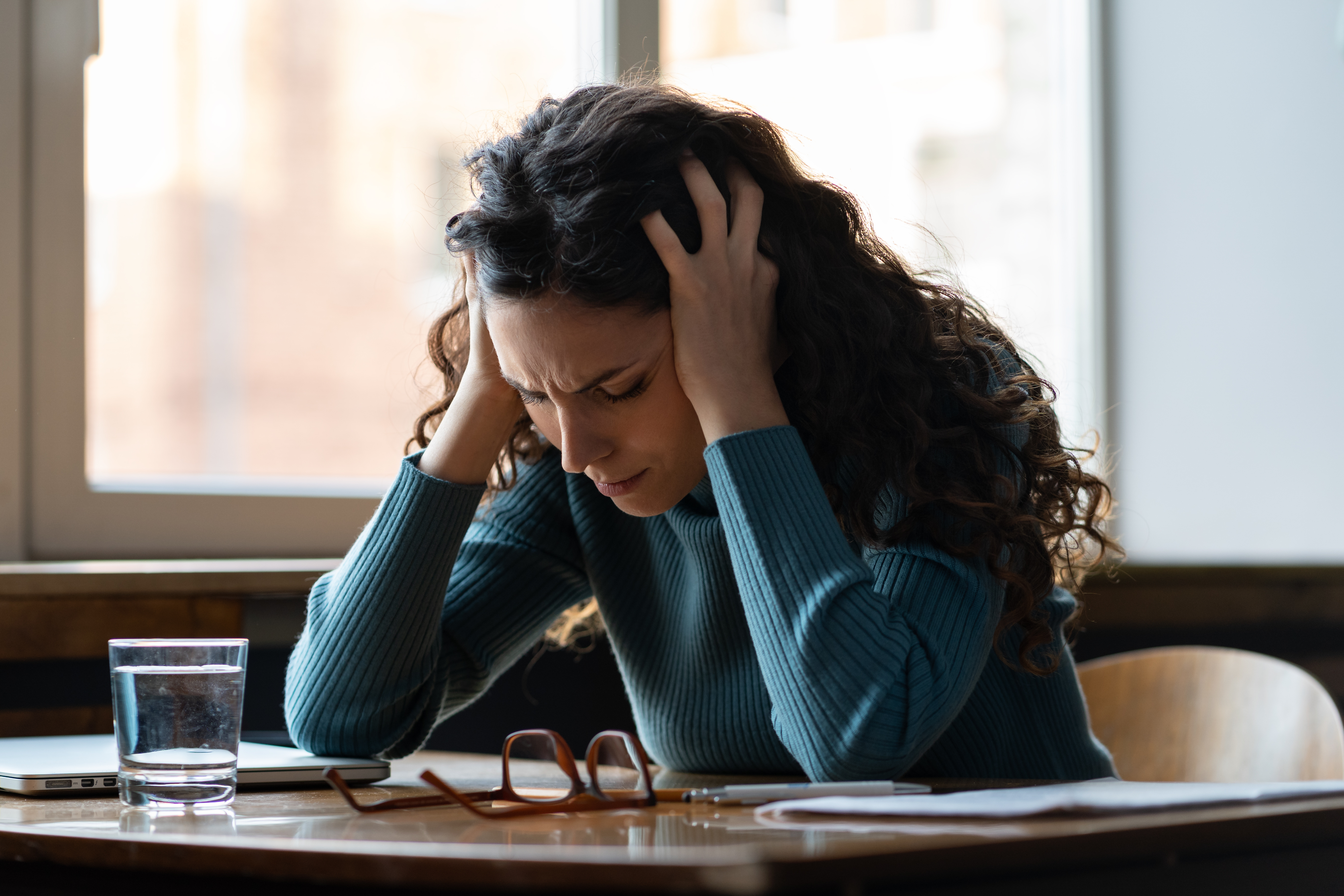 A woman has her hands in her hair in frustration as she looks down at her desk.