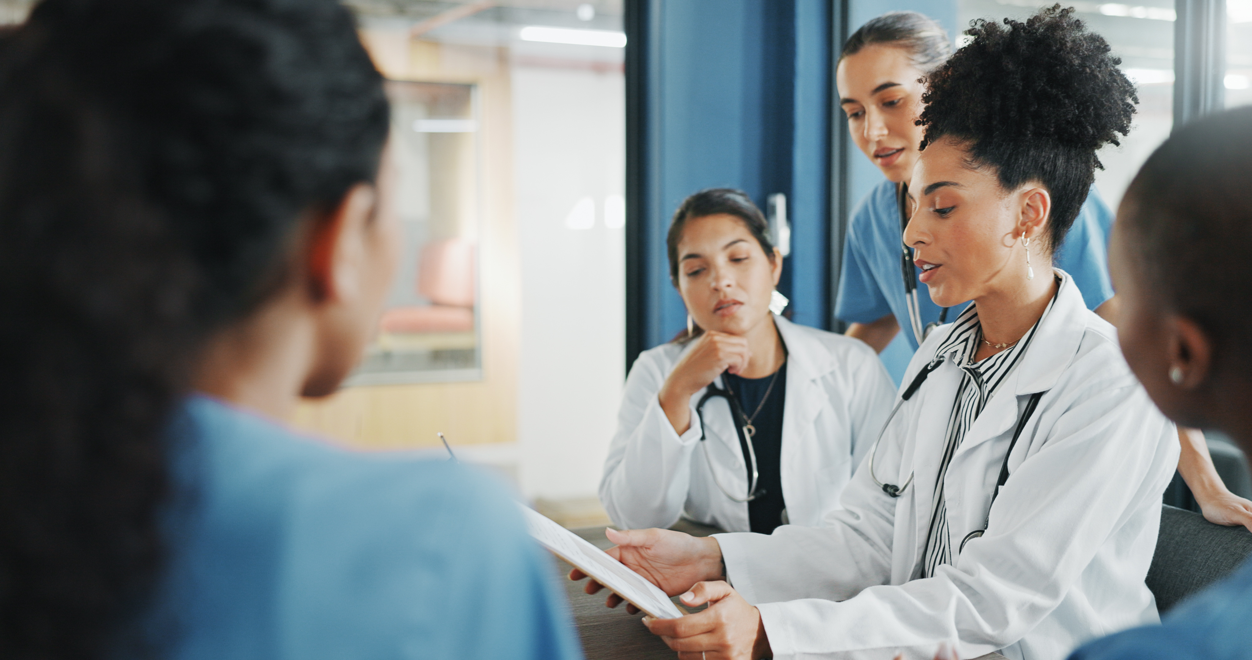 Two doctors and three nurses huddled around a clipboard.