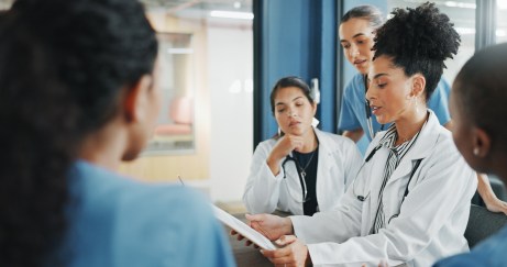 Two doctors and three nurses huddled around a clipboard.