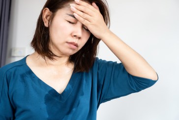 A woman is sweating with her hand on her forehead.