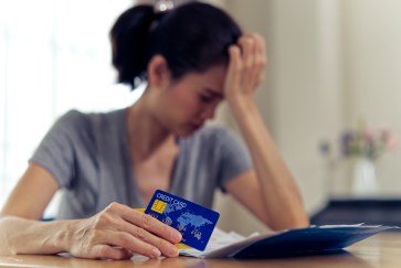 Woman holding hand to head worried holding credit card financial stress