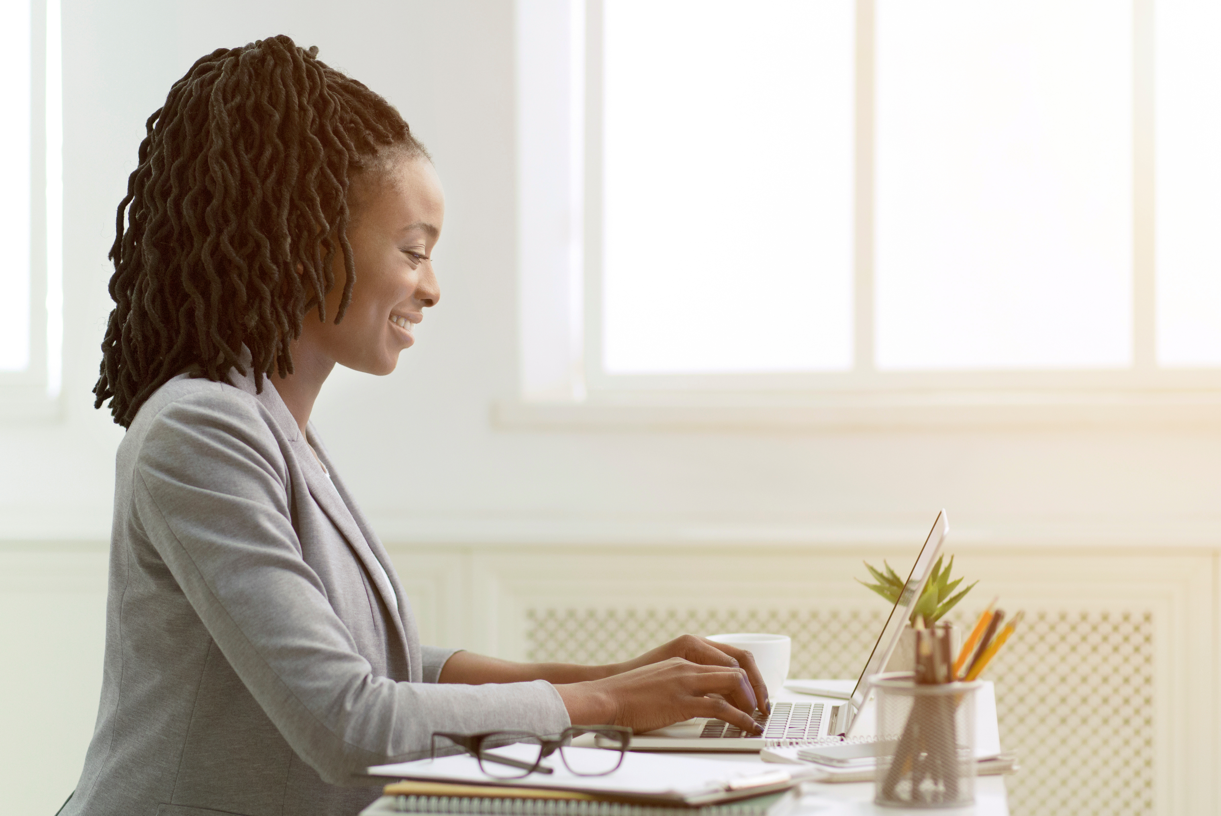 Woman sitting at desk, typing on laptop, smiling