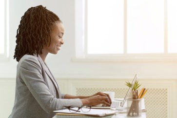 Woman sitting at desk, typing on laptop, smiling